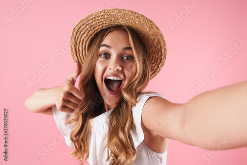 Happy surprised young pretty woman posing isolated over pink wall background showing thumbs up gesture take a selfie by camera.