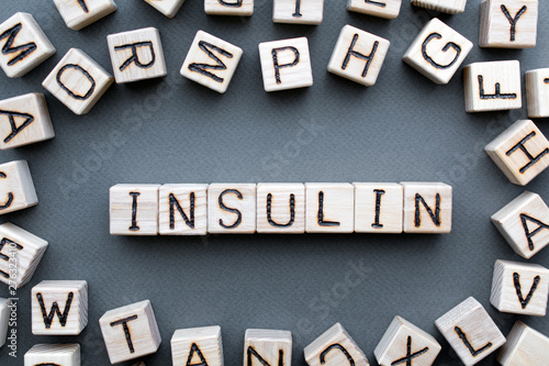 the word insulin wooden cubes with burnt letters, hormone insulin, diabetes treatment  gray background top view, scattered cubes around random letters photo