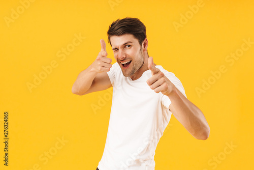 Photo of positive man in basic t-shirt gesturing index fingers on camera meaning hey you photo