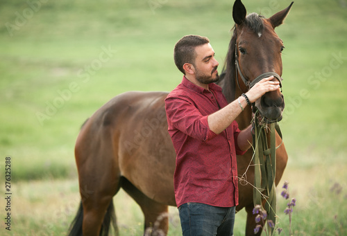 A young man standing on a meadow next to a horse.