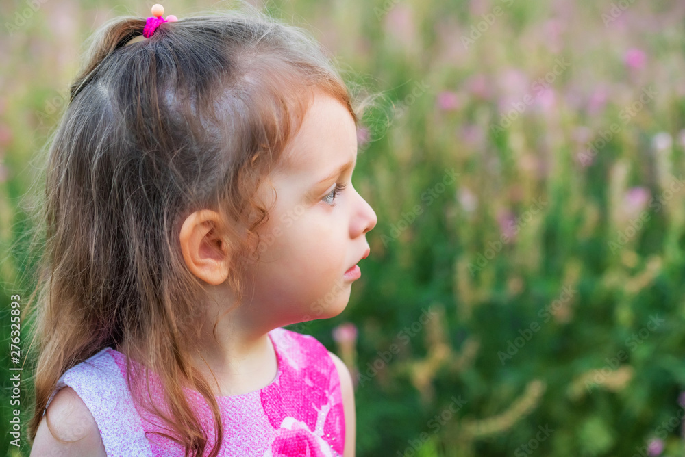Cute serious baby girl looks aside outdoors in green field. Child portrait Cute serious baby girl looks aside outdoors in green field. Child portrait