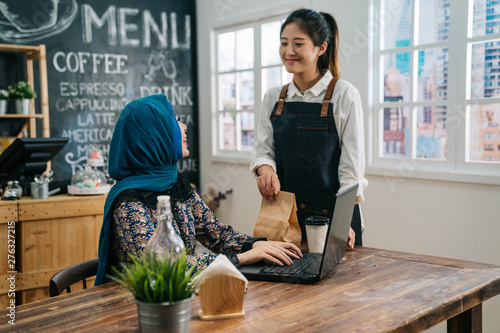 Asian Girl Waitress Staff In Apron Holding Disposable Coffee Cup And Paper Bag In Cafe Bar