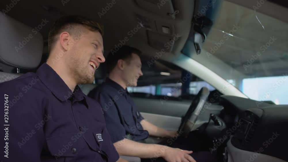 Cheerful police mates laughing in patrol car during daily duty, friendship Cheerful police mates laughing in patrol car during daily duty, friendship