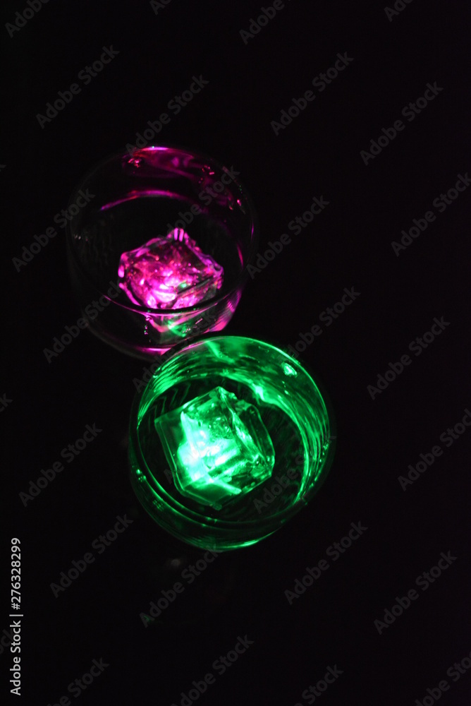 Multicolored glowing ice cubes float in a crystal champagne glass that illuminates the drink in it. Multicolored glowing ice cubes float in a crystal champagne glass that illuminates the drink in it.