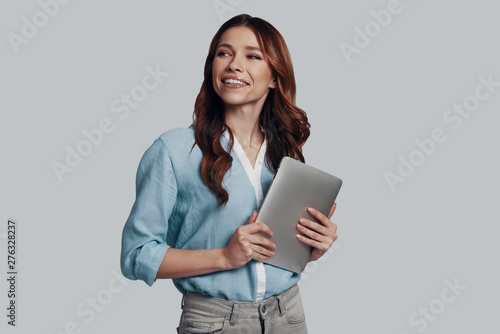 Doing business. Attractive young woman looking away and smiling while standing against grey background