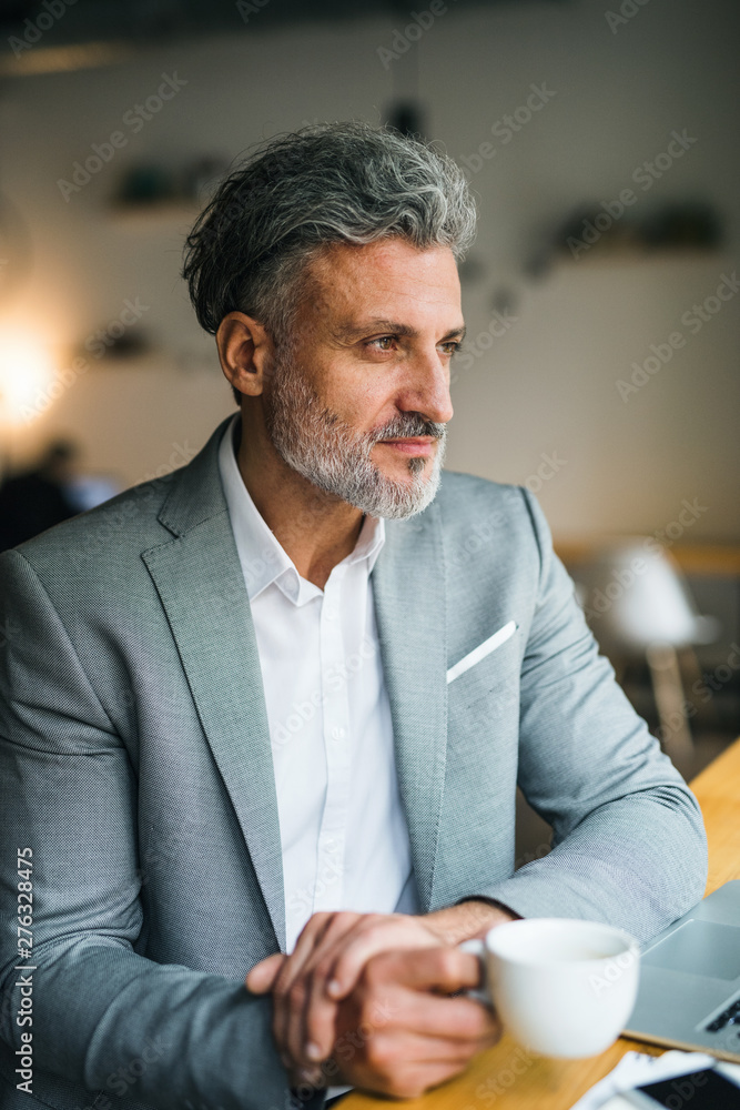 Naklejka premium Mature man with coffee at the table in a cafe, looking out of window.