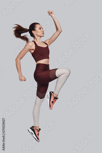 Towards a healthier lifestyle. Full length of attractive young woman in sports clothing jumping while exercising against grey background