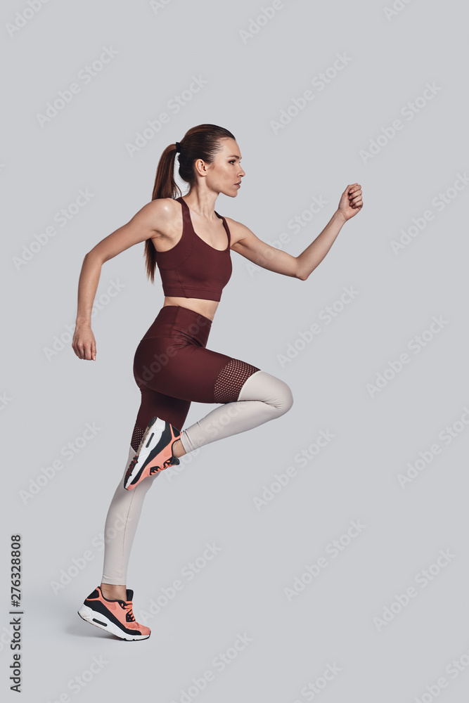 Never stop! Full length of attractive young woman in sports clothing jumping while exercising against grey background