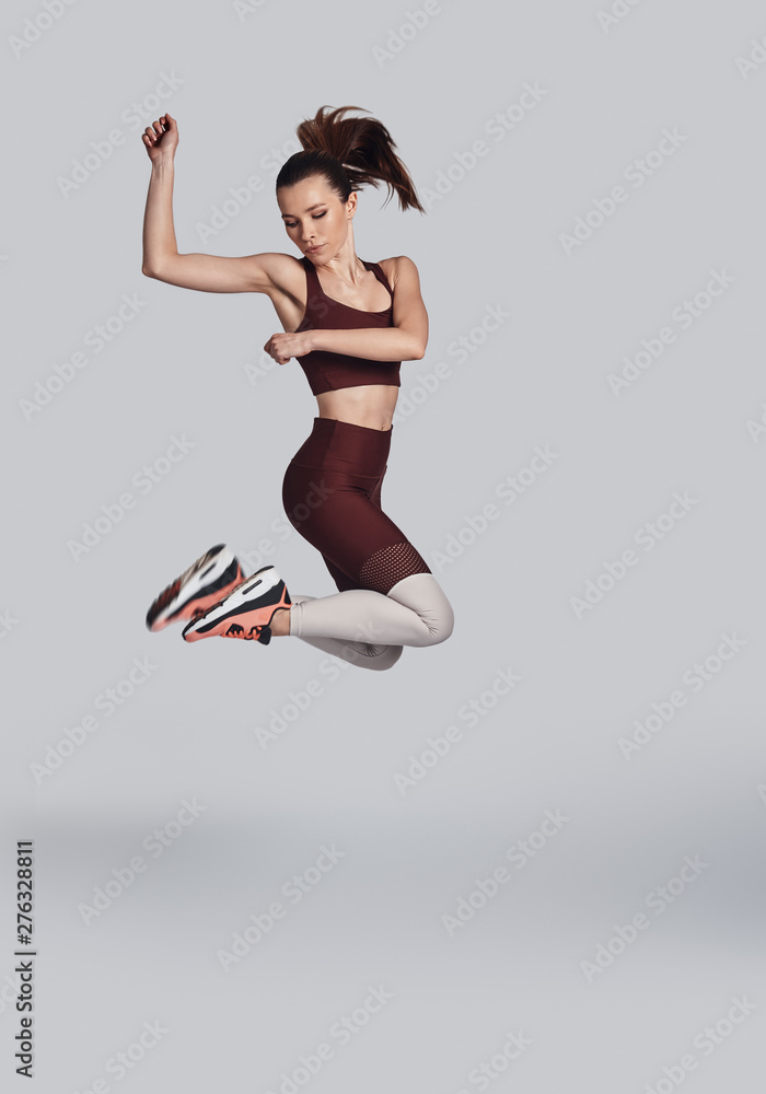 Feeling the freedom. Full length of attractive young woman in sports clothing jumping while exercising against grey background