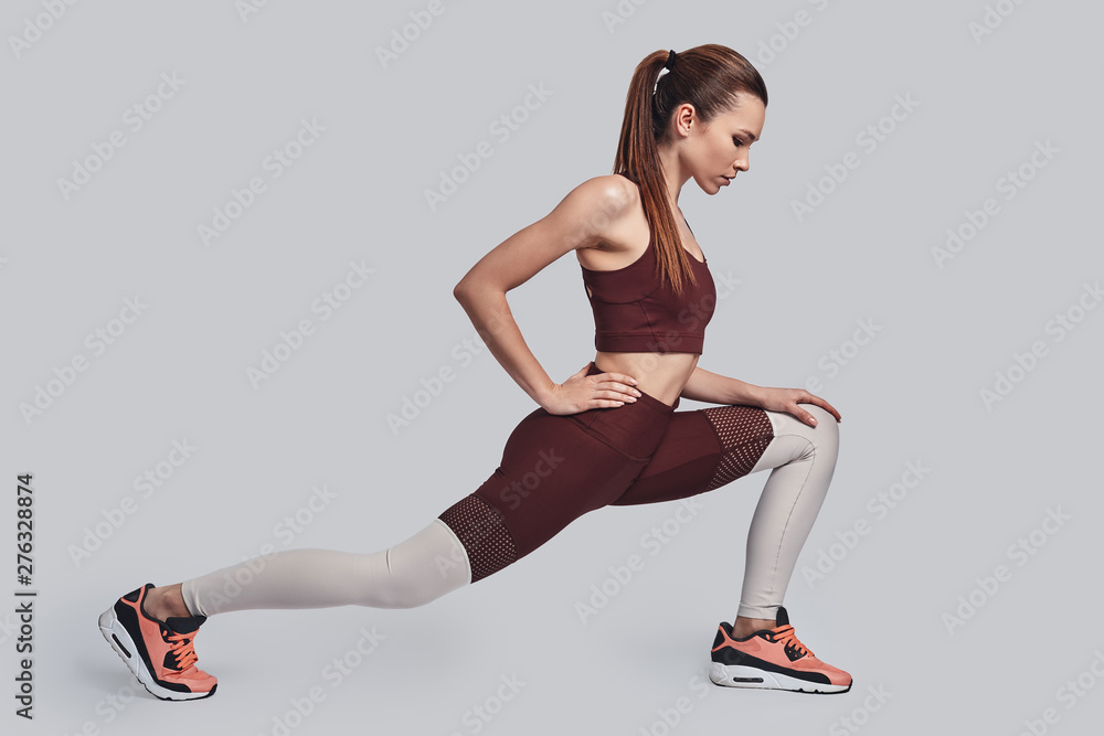 Balance your life. Attractive young woman stretching while exercising against grey background