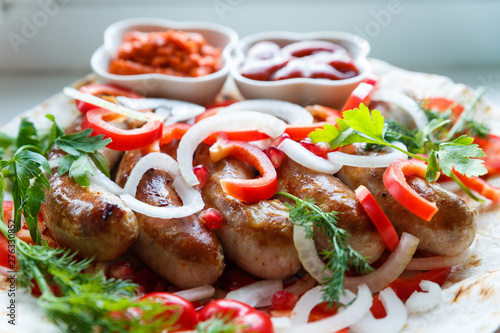 Fried pork sausages on pita bread with ketchup and Armenian appetizer Aivar with vegetables. Lavash, red bell pepper, onions, sausages. Oktoberfest food, the concept of the pub