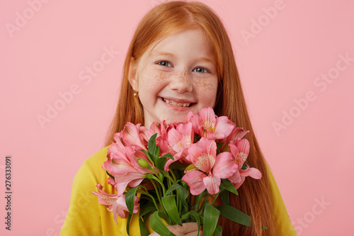 Schilderij op canvas Portrait petite freckles red-haired girl with two tails, broadly smiling and looks cute, holds bouquet, wears in yellow t-shirt, stands over pink background