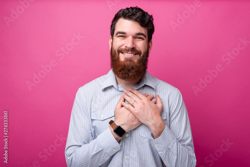 Dear o my heart. Bearded man holds his hands on his heart looking lovely at the camera on pink background.