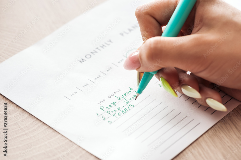 cropped view of woman writing notes on monthly planner, holding green pen in hand cropped view of woman writing notes on monthly planner, holding green pen in hand