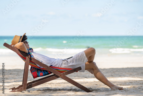 Young asian adult men traveler in casual wear and sun glass relaxing and lying down on colorful beach chair on tropical island beach in summer holidays vacation travel trip with smartphone.