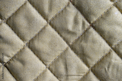 Texture of an aged, rhombic beige bag with a seam and white thread