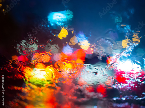 Rain drops on car window with road light bokeh on rainy season abstract background
