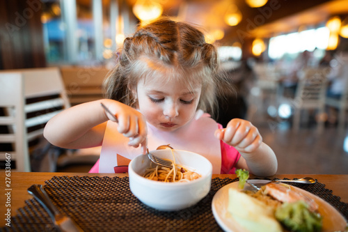 Litle girl is eating pasta in the restaurant.