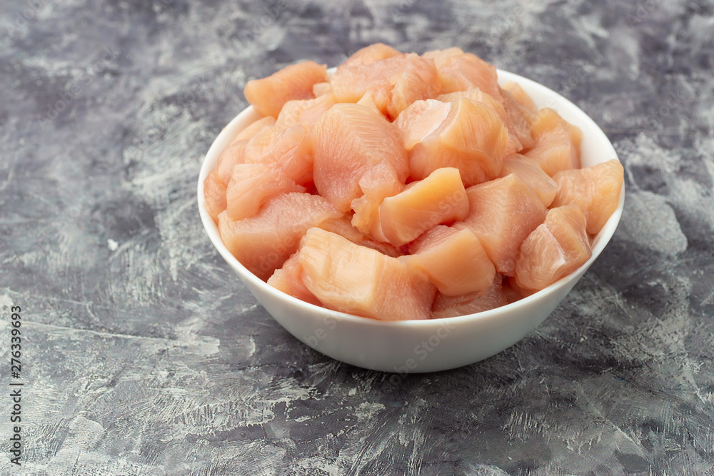 Raw chicken small pieces close up on grey marble background Raw chicken small pieces close up on grey marble background