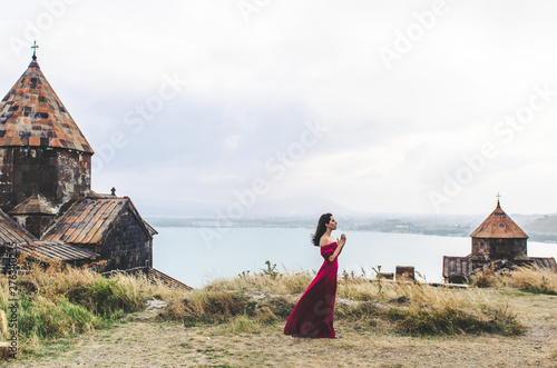 Portrait of young woman in red dress standing near monastery and pray, Armenia