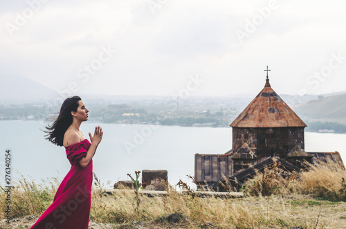 Portrait of young woman in red dress standing near monastery and pray, Armenia