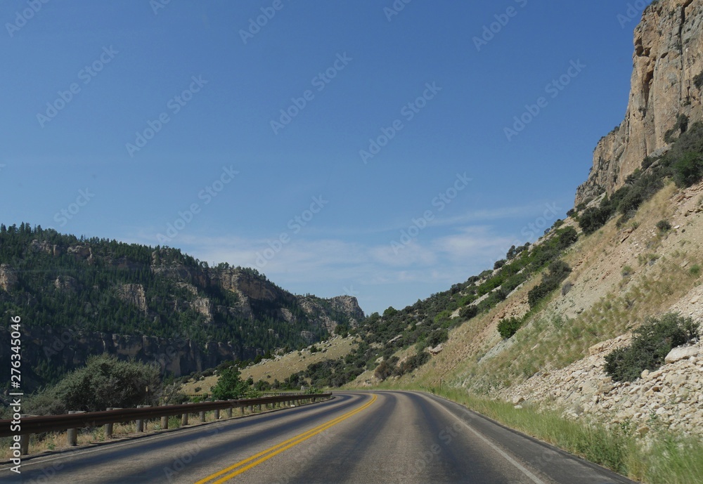 Wide scenic view of a winding road with geologic formations and cliffs through the Bighorn Mountains in Wyoming, USA.