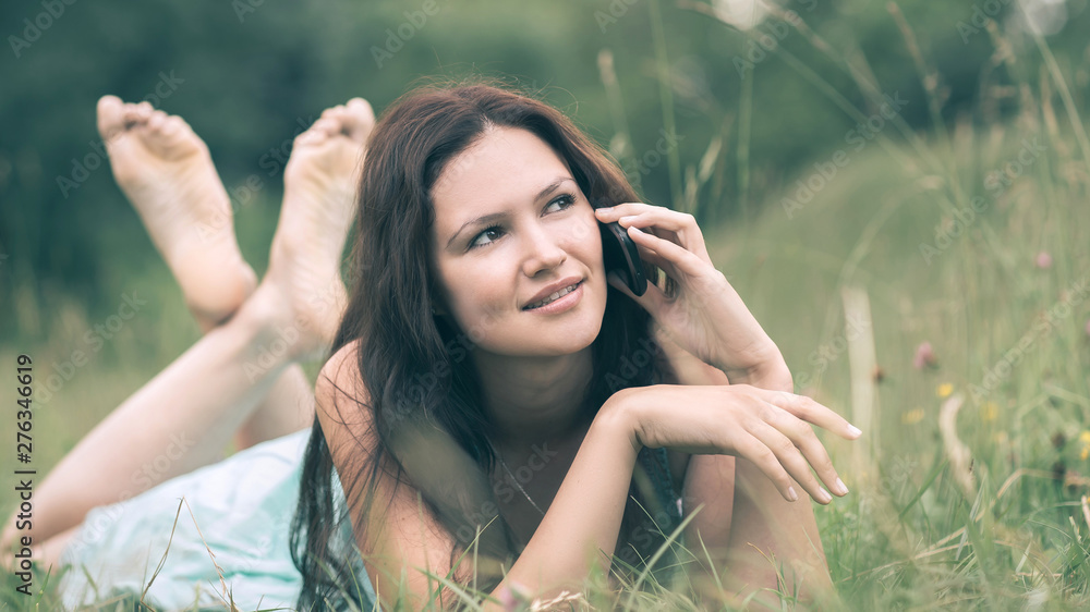 charming girl talking on a smartphone, lying on the grass on a summer day charming girl talking on a smartphone, lying on the grass on a summer day