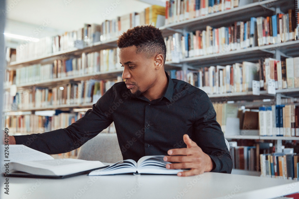 Having research. African american man sitting in the library and searching for some information in the books Having research. African american man sitting in the library and searching for some information in the books