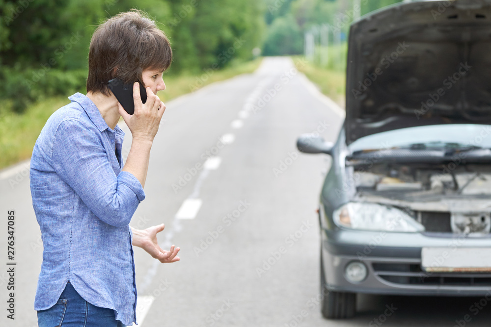 Worried woman talks on the phone near her old broken car on the road Worried woman talks on the phone near her old broken car on the road