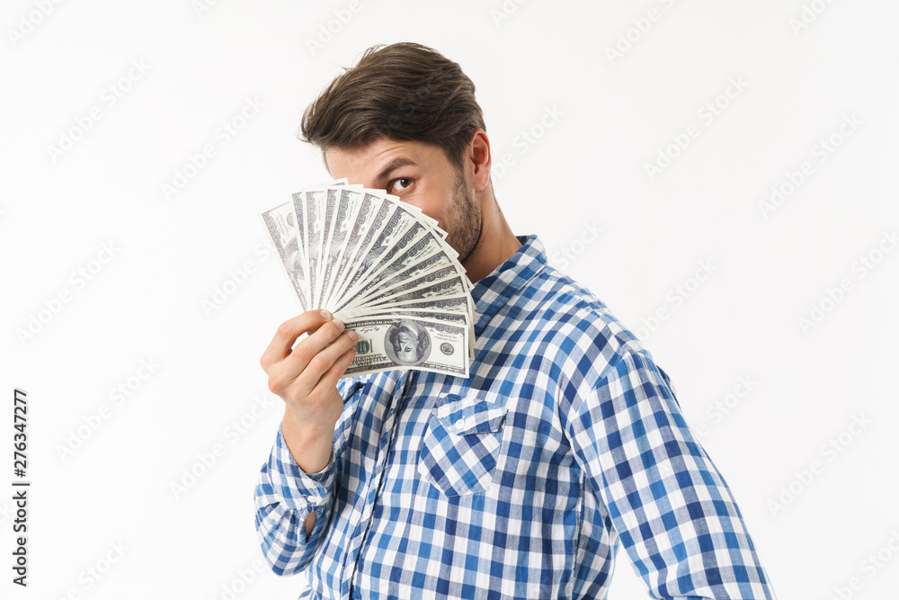 Bearded unshaved man dressed in casual shirt posing isolated over white wall background holding money covering face. Bearded unshaved man dressed in casual shirt posing isolated over white wall background holding money covering face.