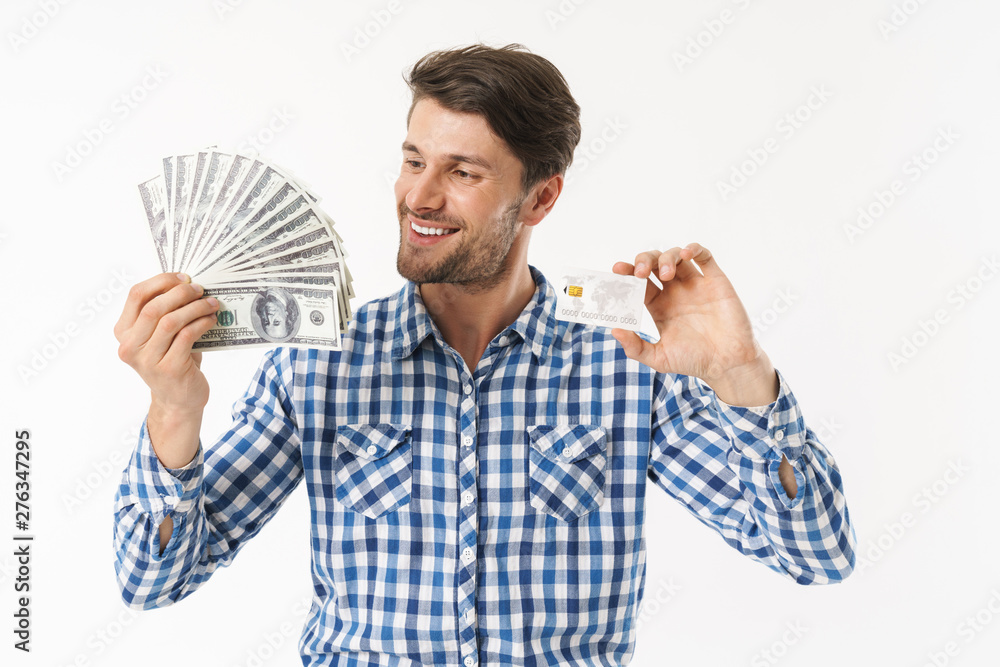Happy cheerful bearded unshaved pleased man dressed in casual shirt posing isolated over white wall background holding money and credit card. Happy cheerful bearded unshaved pleased man dressed in casual shirt posing isolated over white wall background holding money and credit card.