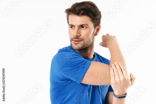 Concentrated young sports fitness man standing isolated over white wall background make stretching exercises for arms triceps.