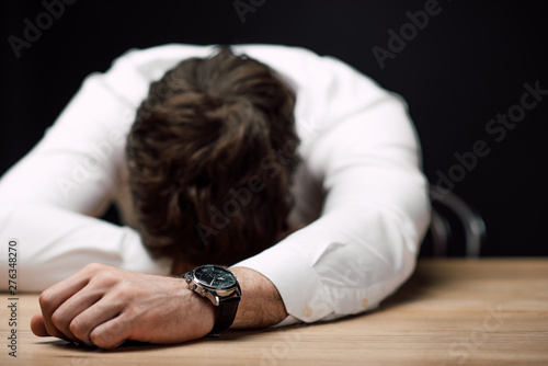 drunk, exhausted businessman lying on wooden table isolated on black photo