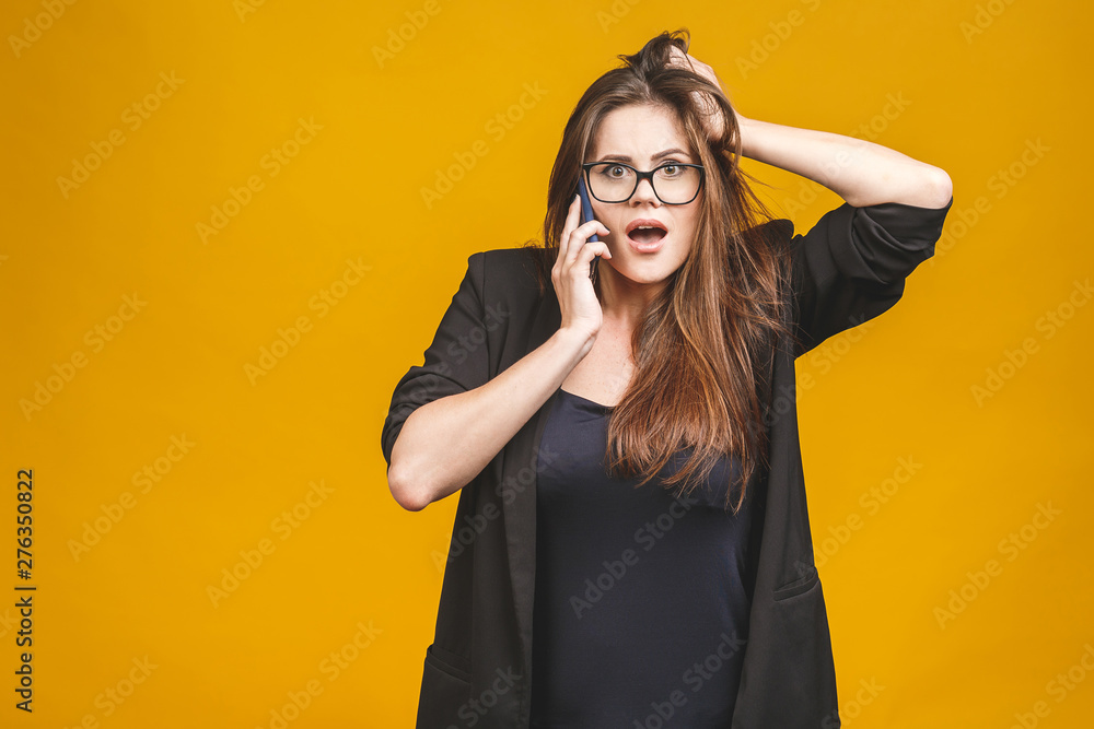Portrait of a happy amazed woman in smart casual talking on the phone over yellow background. Portrait of a happy amazed woman in smart casual talking on the phone over yellow background.