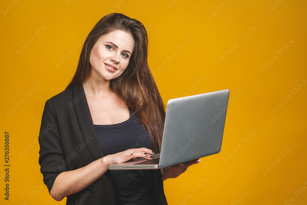 Young happy smiling woman in casual clothes holding laptop and sending email to her best friend isolated against yellow background. Young happy smiling woman in casual clothes holding laptop and sending email to her best friend isolated against yellow background.
