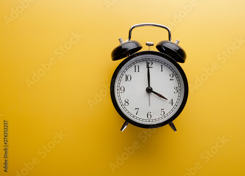 Alarm clock on yellow background top view. Concept of time.