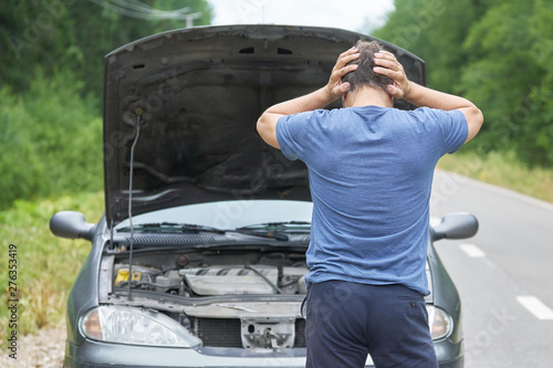 Middle-aged worried man stands with his hands on the head near his broken car with raised hood on the rural road photo