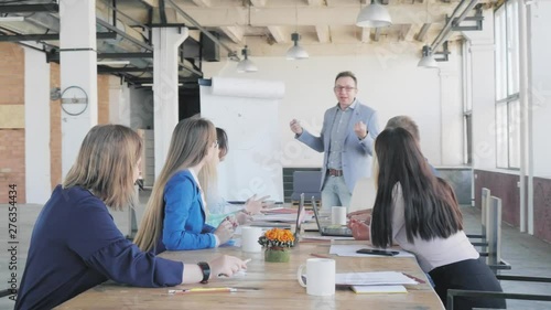 Business team fun discussing a presentation. A male manager answers questions from employees who sit at a large table near a flipchart. Office life. Coworking