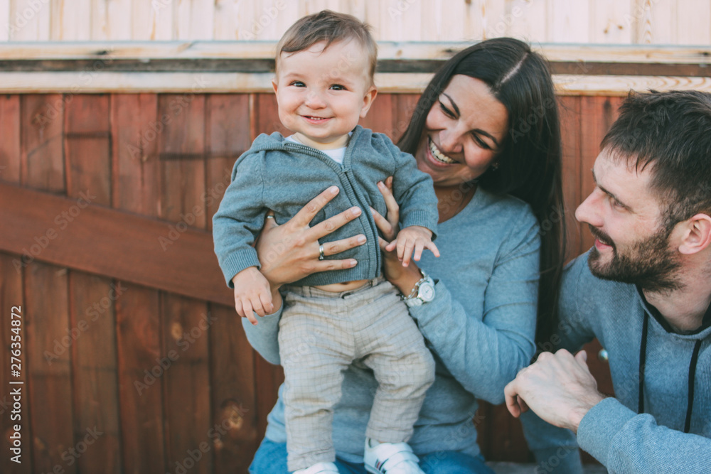 Happy family with cute baby boy on wooden house background outdoors, country life nature concept Happy family with cute baby boy on wooden house background outdoors, country life nature concept