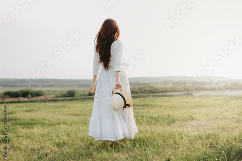 Beautiful carefree long hair girl in white clothes and straw hat enjoys life in nature field at sunset. Sensitivity to nature concept