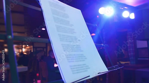 Slow hitting the music stand with white sheets of paper standing on the club's stage, the faces of the visitors blurred