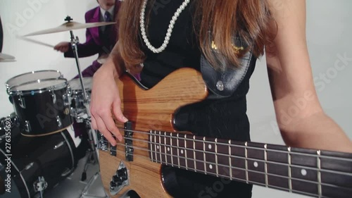 Bass player-girl in black dress and beads plays solo slowly, fingers on strings