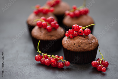 Chocolate muffins decorated red currant berries on dark wooden background. Flat lay. Soft focus