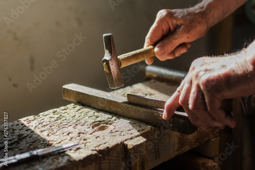 Hands of an elderly man working on the iron with the hammer.