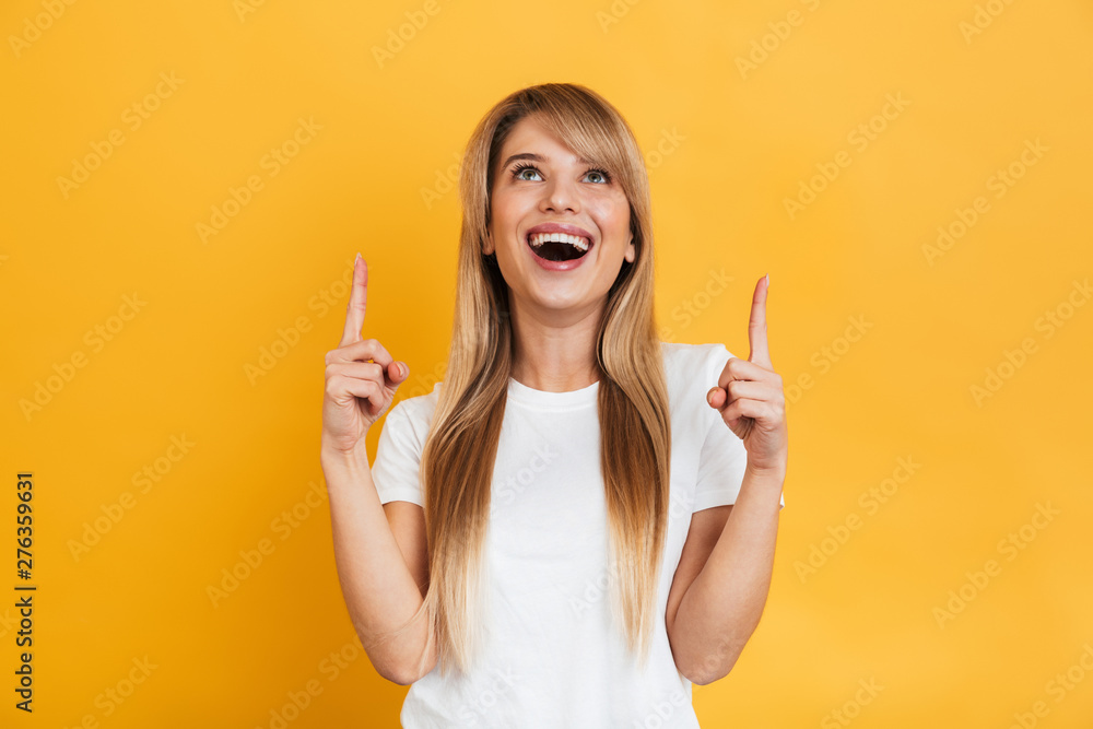 Surprised young excited shocked blonde woman posing isolated over yellow wall background pointing. - obrazy, fototapety, plakaty 