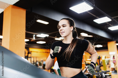 Enduring serious young woman triathlete runs on a treadmill after strength training in the gym. Concept of skinny and fat burning