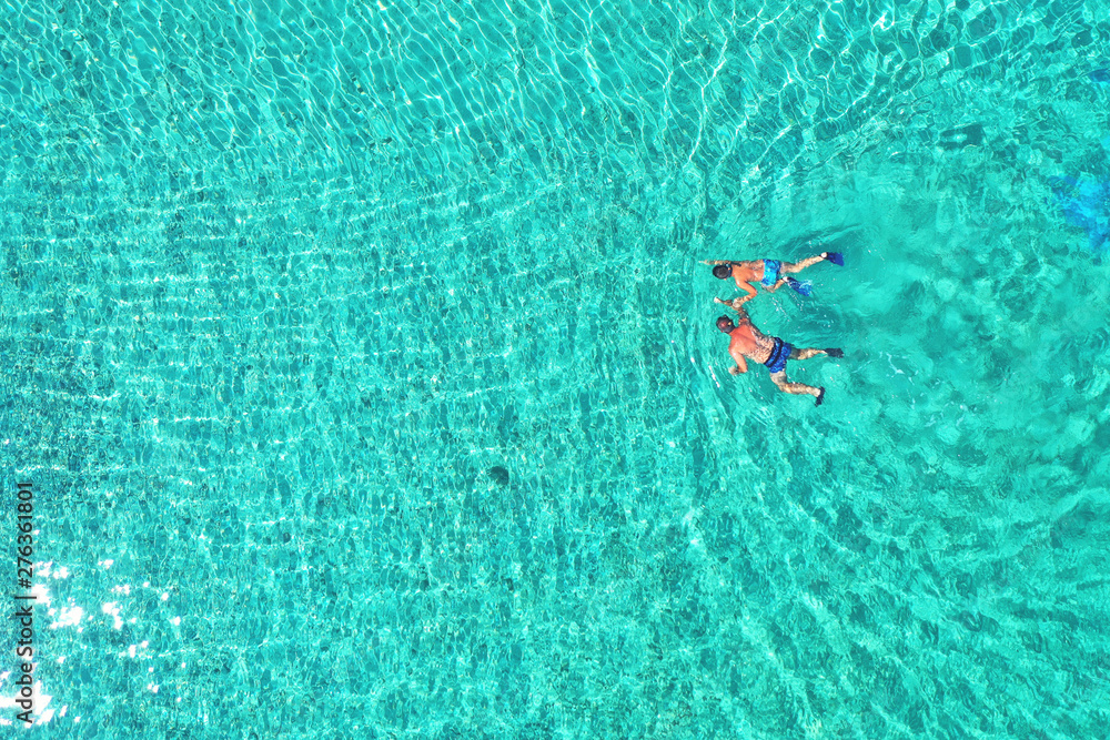 Father and son snorkels through tropical, turquoise waters, aerial view