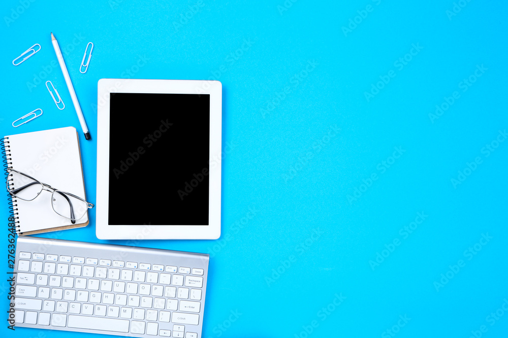 Tablet, keyboard computer with glasses and notepad on blue background Tablet, keyboard computer with glasses and notepad on blue background