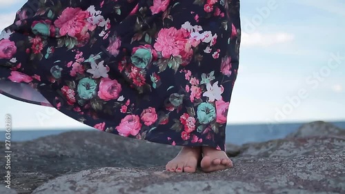 Female well-groomed legs close up on a stone, a woman moves her legs, a dress develops in the wind.