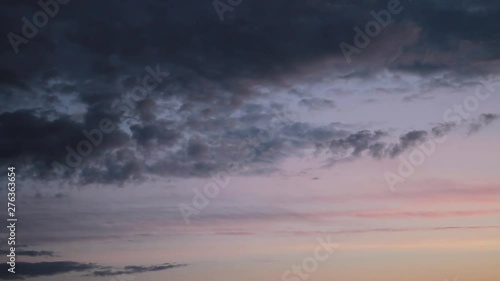 Gray rain clouds float across the blue sky at sunset.
